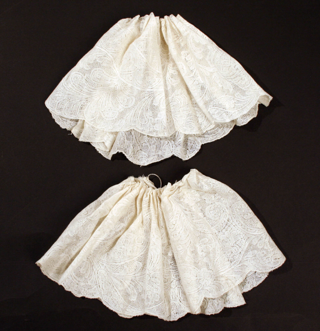 Zwei weiße Spitze-Röcke mit zarten Mustern auf schwarzem Hintergrund.