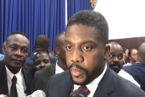 Ein Mann im Anzug und Krawatte spricht in ein Mikrofon vor einem Publikum, mit Vorhängen und einer Wand im Hintergrund, wahrscheinlich bei der Ankündigung seiner lebenslangen Haftstrafe.