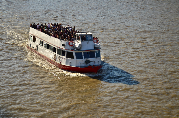 A ship sails on the water with many people on its deck.