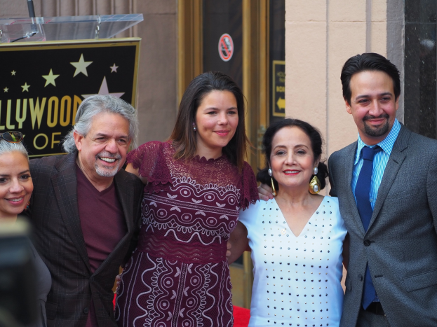 Eine Gruppe von Menschen, die auf einem roten Teppich stehen, lächeln und für ein Foto posieren, mit einer Tafel mit Text, einem Glaspodest und einer Wand im Hintergrund und einer Kamera auf der linken Seite.
