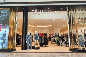 Ein stylischer Mode-Boutique in einem Einkaufszentrum, mit Schaufensterpuppen in der neuesten Mode, Kleidung an Bügeln, einer Säule, einem Schild mit Text und einer Fliesenboden.