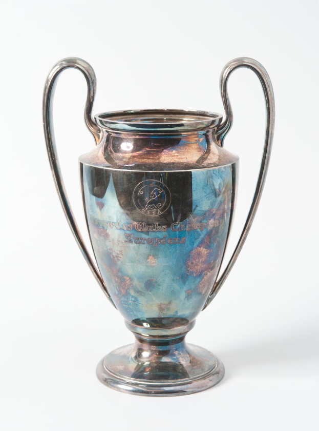 Der UEFA-Champions-League-Pokal, ein stählerner Becher mit zwei Griffen und einem blauen und silbernen Farbschema, mit der Inschrift 'UEFA Champions League', gegen einen weißen Hintergrund dargestellt.