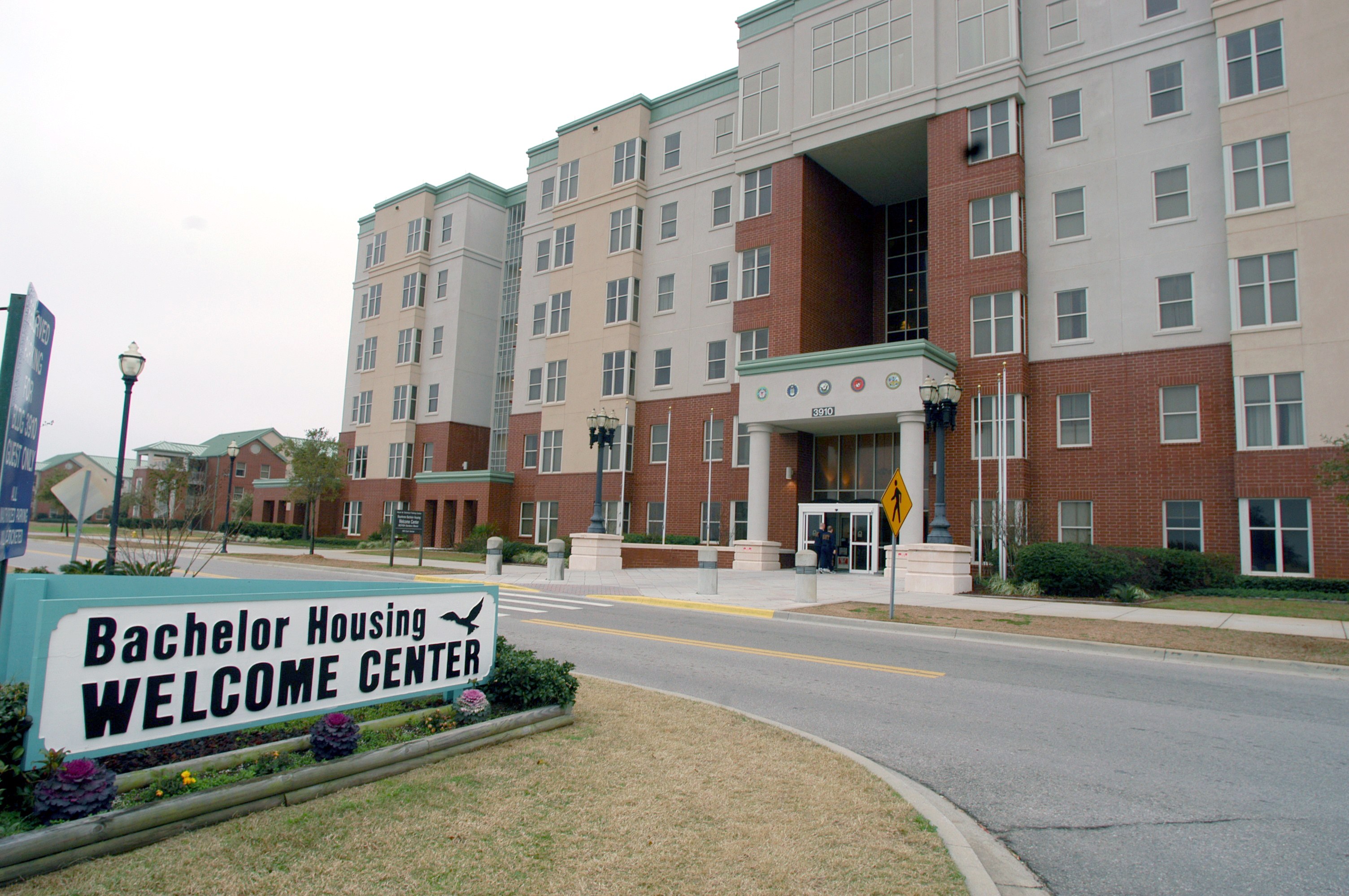 Ein Willkommenszentrum für Bachelor-Unterkünfte mit Gebäuden, Straßeneinrichtungsgegenständen, Fahrzeugen, Grünflächen und einem klaren Himmel.