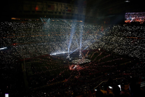 Eine gro├če Menge Menschen in einem Stadion bei Nacht, beleuchtet von hellen Lichtern, mit einem Bildschirm auf der rechten Seite, der wahrscheinlich die Ergebnisse der Super Bowl XLVII-Halbzeitenshow anzeigt.