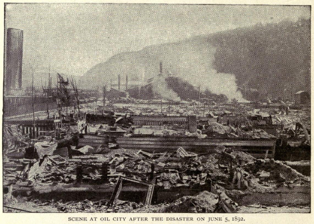 Schwarz-weiß-Foto einer Stadt nach einer Katastrophe am 5. Juni 1892, das Gebäude, Masten, Rauch und einen Hügel im Hintergrund zeigt.