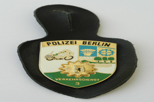 Ein schildförmiges Polizeibadge mit der Aufschrift "Polizei Berlin" auf blauem Hintergrund, einem weißen Stern und einem weißen Rand, das auf einer Oberfläche liegt.