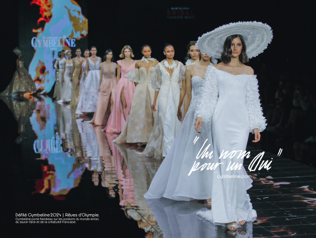 Eine Gruppe von Frauen in weißen Kleidern und Hüten läuft über den Laufsteg mit dunklem Hintergrund und einem Bildschirm, während Zuschauer auf der rechten Seite sitzen und Text am unteren Rand 'Cymbeline Bridal Fashion Week 2020' angezeigt wird.