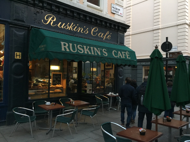 Eine Gruppe von Menschen steht vor einem Café mit einem Schild, auf dem "Ruskins Café" steht.