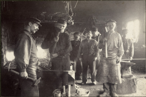 Eine Gruppe von Männern in einer Schmiede, jeder hält einen Hammer, auf einem Schwarz-Weiß-Bild.