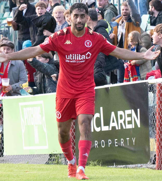 Ein Fussballspieler in roter Uniform rennt mit ausgestreckten Armen auf einem Feld, mit einer Menge im Hintergrund und einem Banner mit der Aufschrift "Middlesbrough FC vs. Swansea City - Sky Bet Championship" im Vordergrund.