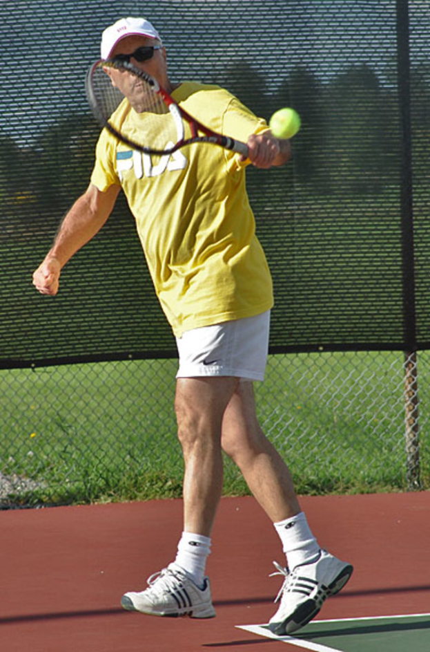 Ein Mann mit Brille, T-Shirt, Mütze und Schuhen spielt Tennis.