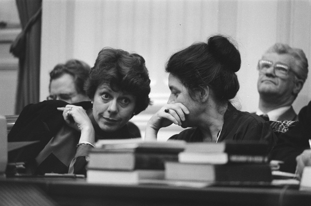 Schwarz-weißes Bild von zwei Frauen an einem Tisch in einem Gerichtssaal; eine scheint Richterin zu sein, die andere eine Teilnehmerin, mit Büchern und rechtlichen Gegenst├Ąnden drumherum.