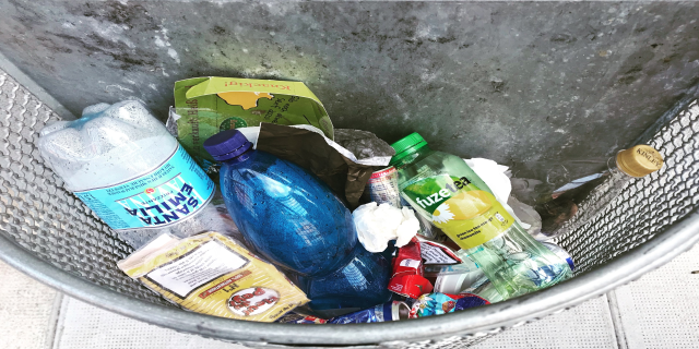 Ein Metallmüllcontainer voller Plastikflaschen, Tüten und anderen Gegenständen.