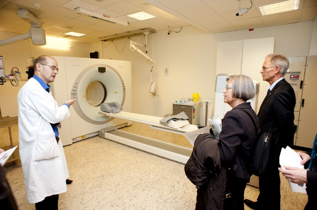Arzt in weißer Uniform erklärt CT-Scan-Maschine zwei Menschen in schwarzen Mänteln
