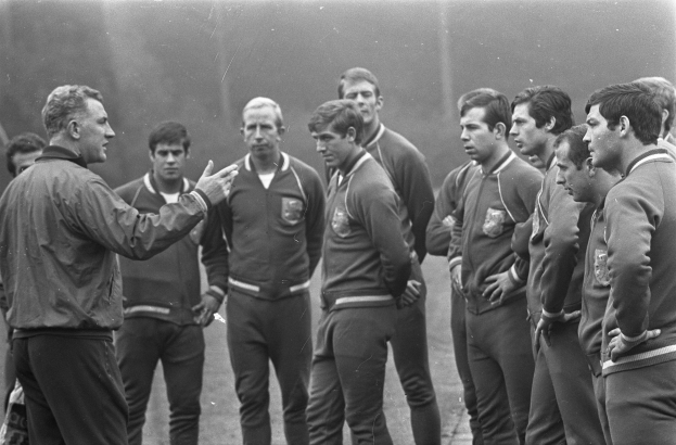 Ein Schwarz-Weiß-Foto von einer Gruppe Männer auf einem Fussballfeld, wobei der Mann in der Mitte einen Walking-Schuh trägt.