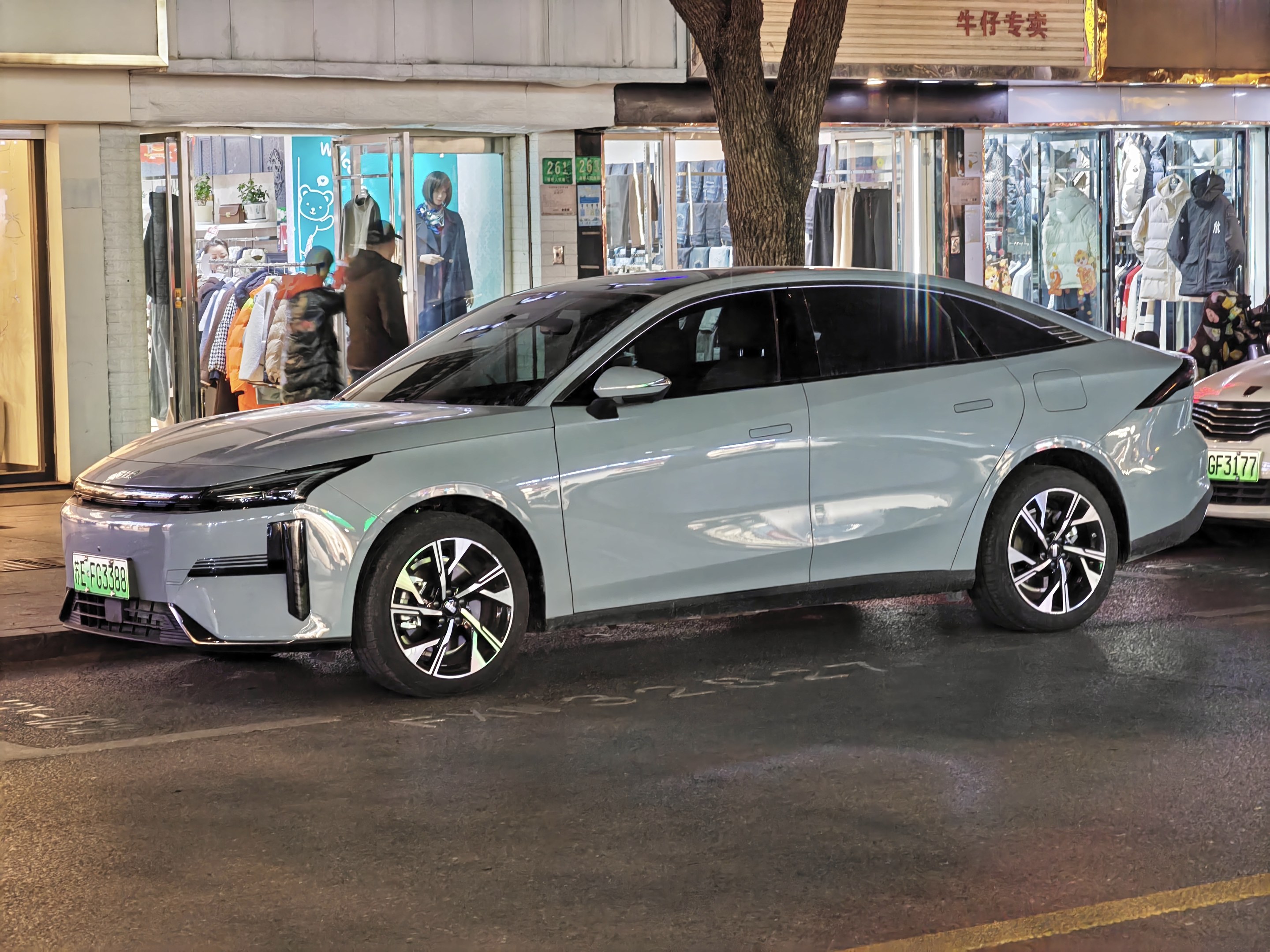 Elektrischer Mitsubishi Lancer EV auf einer nächtlichen Straße geparkt, umgeben von Gebäuden, beleuchteten Schaufenstern, Schaufensterpuppen und Schildern.