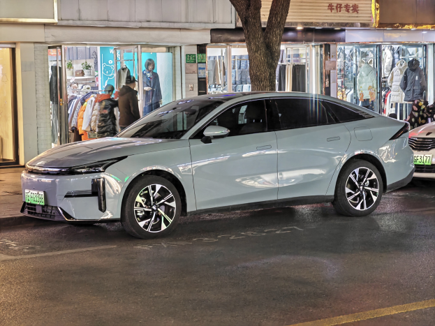 Elektrischer Mitsubishi Lancer EV auf einer nächtlichen Straße geparkt, umgeben von Gebäuden, beleuchteten Schaufenstern, Schaufensterpuppen und Schildern.