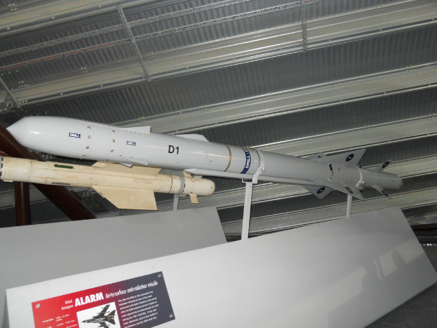 Raketen werden mit weißen Tafeln am Boden gezeigt, von denen eine ein rotes und graues Plakat mit Text in der linken unteren Ecke hat und ein weißes Dach oben.