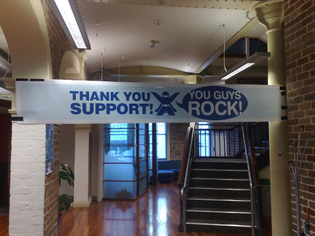Ein Dankeschön-Banner ist an einer Wand und einer Säule vor einer Treppe befestigt, mit Fenstern im Hintergrund.
