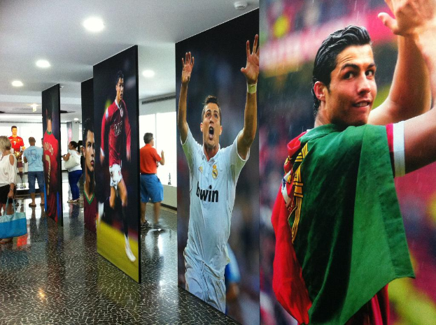 Ein Banner mit dem Fußballspieler Rolando, auf dem Menschen links neben einem Tisch und Lampen oben zu sehen sind.