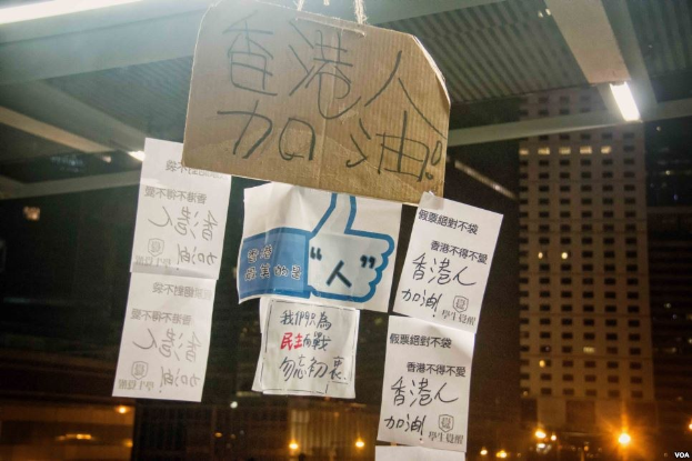 Gruppe von Menschen vor einem beleuchteten Gebäude an einem dunklen Abend mit Protestschildern an der Decke.