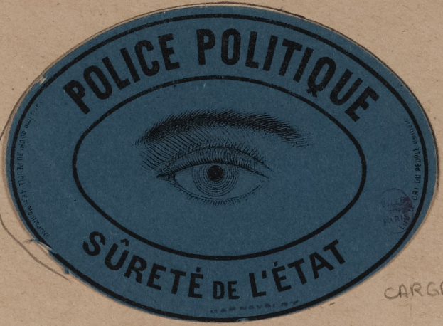 Brauner Karton mit einem blauen Aufkleber mit der Aufschrift "Polizei Politique Surete de L'Etat" und einem Auge-Symbol.