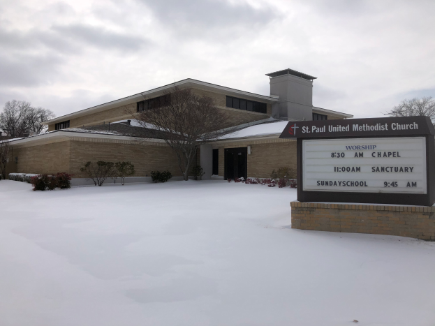 St. Paul United Methodist Church, a building with windows and doors, surrounded by plants and trees, with snow on the ground and a cloudy sky in the background, with a board with text on the right side.