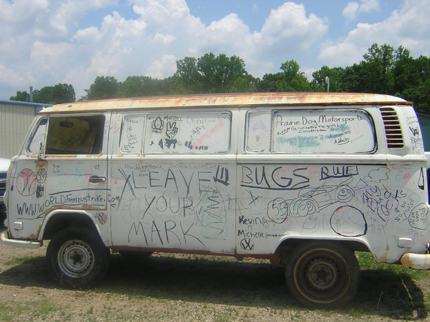 Ein beschädigtes Auto mit Gemälden und Zitaten darauf, das vor einem bewaldeten Gebiet geparkt ist.
