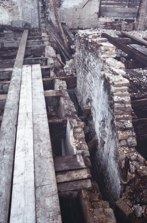Altbau im Abriss mit verstreuten Holzplanken und Steinen im Vordergrund, Ziegelwand im Hintergrund sichtbar.