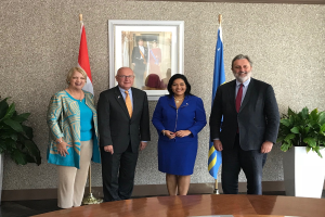 Eine Gruppe strahlender Menschen um einen Tisch mit Papieren herum, umgeben von Fahnen, Topfpflanzen und einem Fotorahmen an der Wand, feiert die Unterzeichnung eines Memorandums von Verständnis zwischen den Vereinigten Staaten und Kanada.