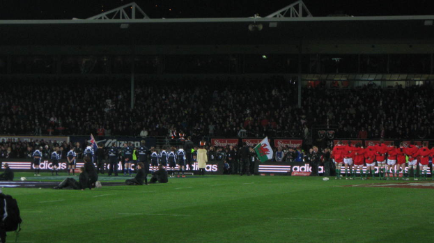 Eisernes Gitter und Lautsprecher an der Spitze eines Stadions mit einer Menge, Werbung, Flagge und Boden darunter.