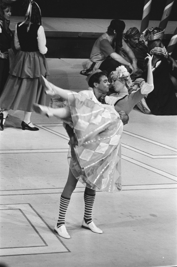 Schwarzes und weißes Foto von zwei Menschen, die auf einer Bühne tanzen, mit einigen Sitzenden im Hintergrund und einem Pfahl im Vordergrund.