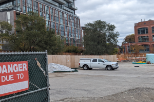 Truck parked in front of a building with a "Danger Due to Open Excavation" sign, trees and buildings in the background under a clear blue sky.