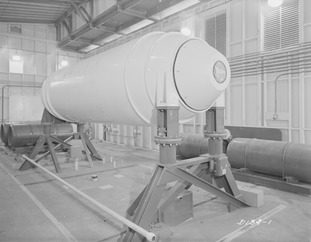 Großer zylindrischer Wasserstoffbomben auf einem Ständer in einer Fabrik mit Rohren, Lampen und einer Wand im Hintergrund.