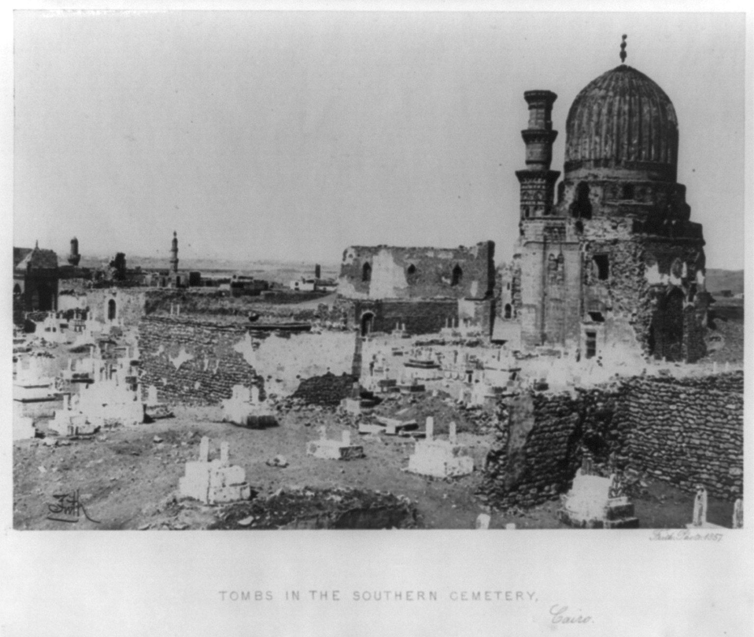 Ein Schwarz-Weiß-Foto eines Friedhofs mit Grabsteinen, einer Moschee im Hintergrund und Text unten.