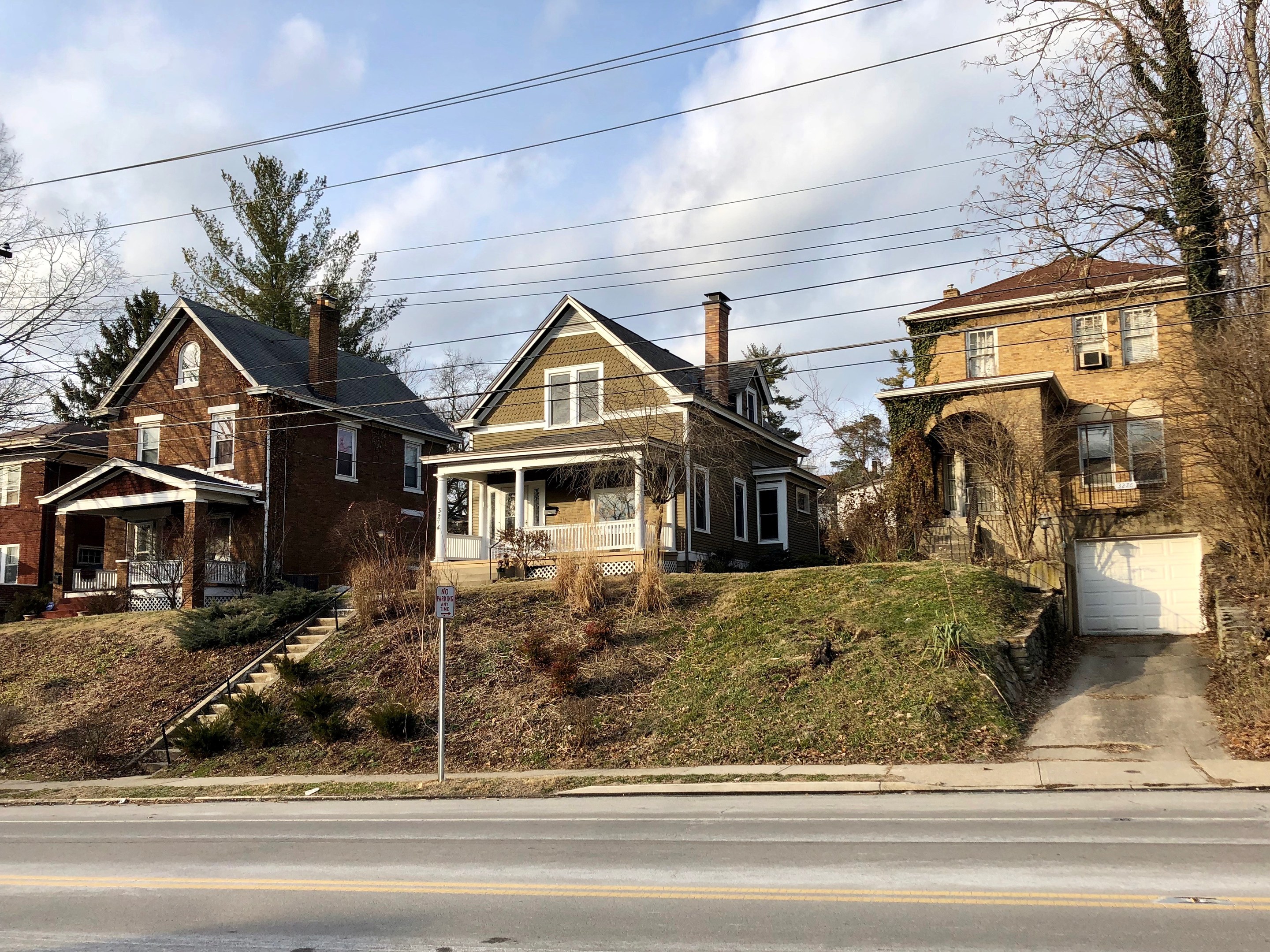 Reihe von Häusern entlang einer Straße mit Fenstern, Türen, Säulen, Geländern, Stufen, Pflanzen, Gras, Bäumen und einem Wegweiser unter einem bewölkten Himmel, repräsentiert eines der teuersten Häuser zum Verkauf in Detroit.