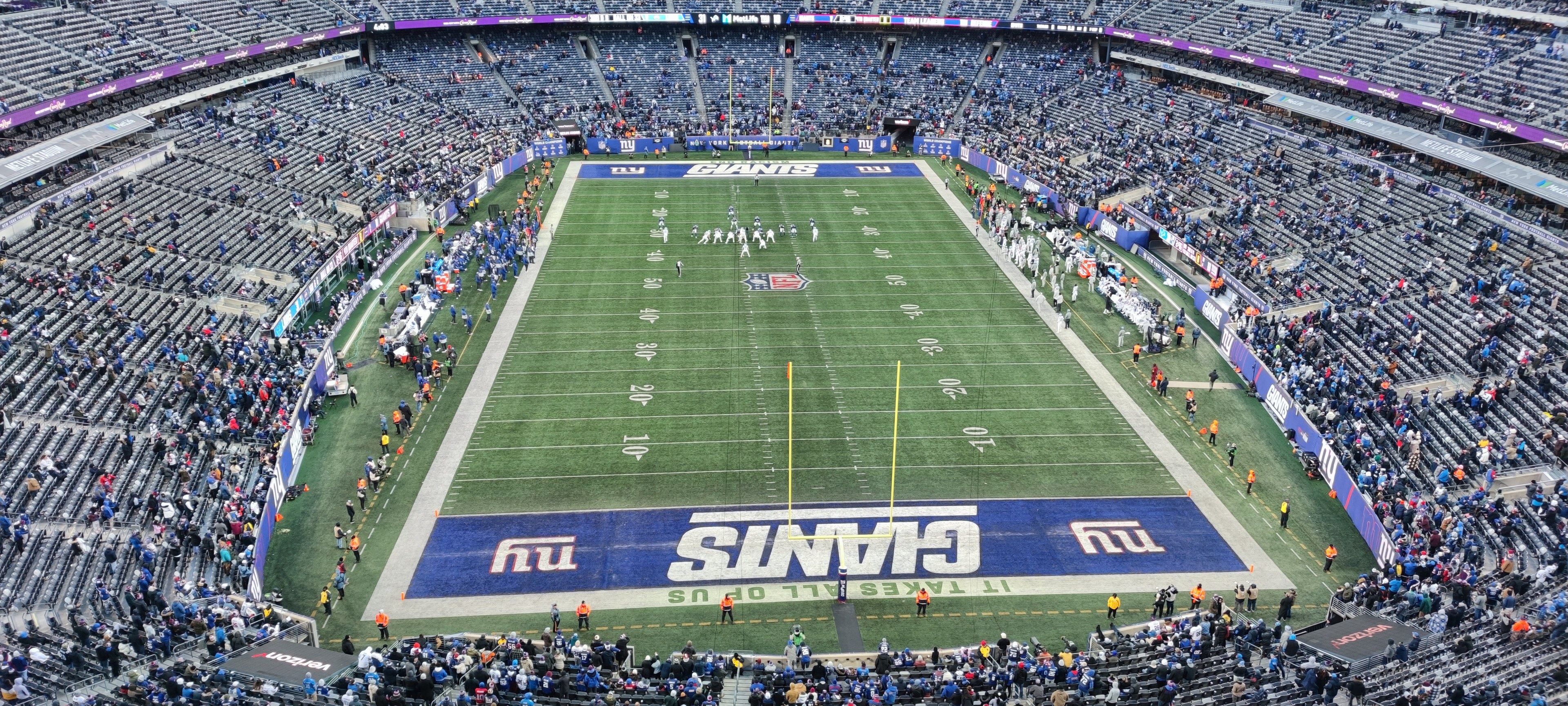 Ein voller Fußballstadion mit Spielern auf dem Feld, Torpfosten und Zuschauern auf den Sitzen unter einer lebendigen Atmosphäre.